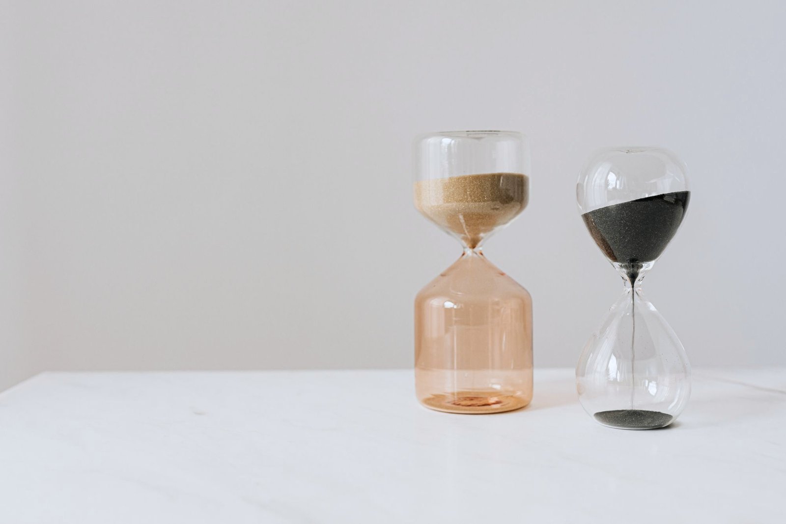 Two hourglasses side by side, one with pale sand and one with dark