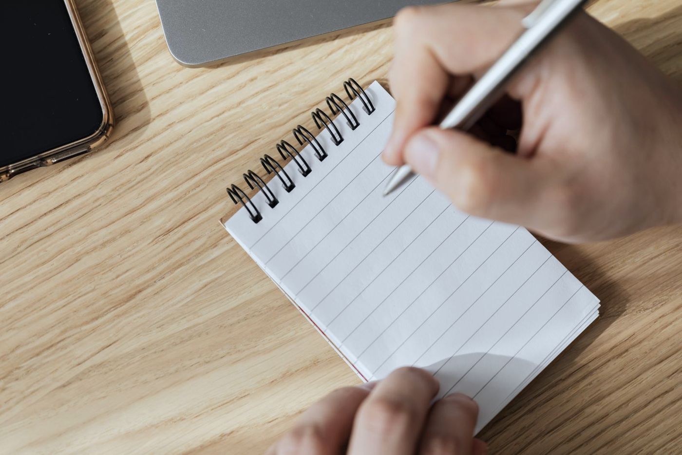 Writing a note on a notepad beside a laptop and phone